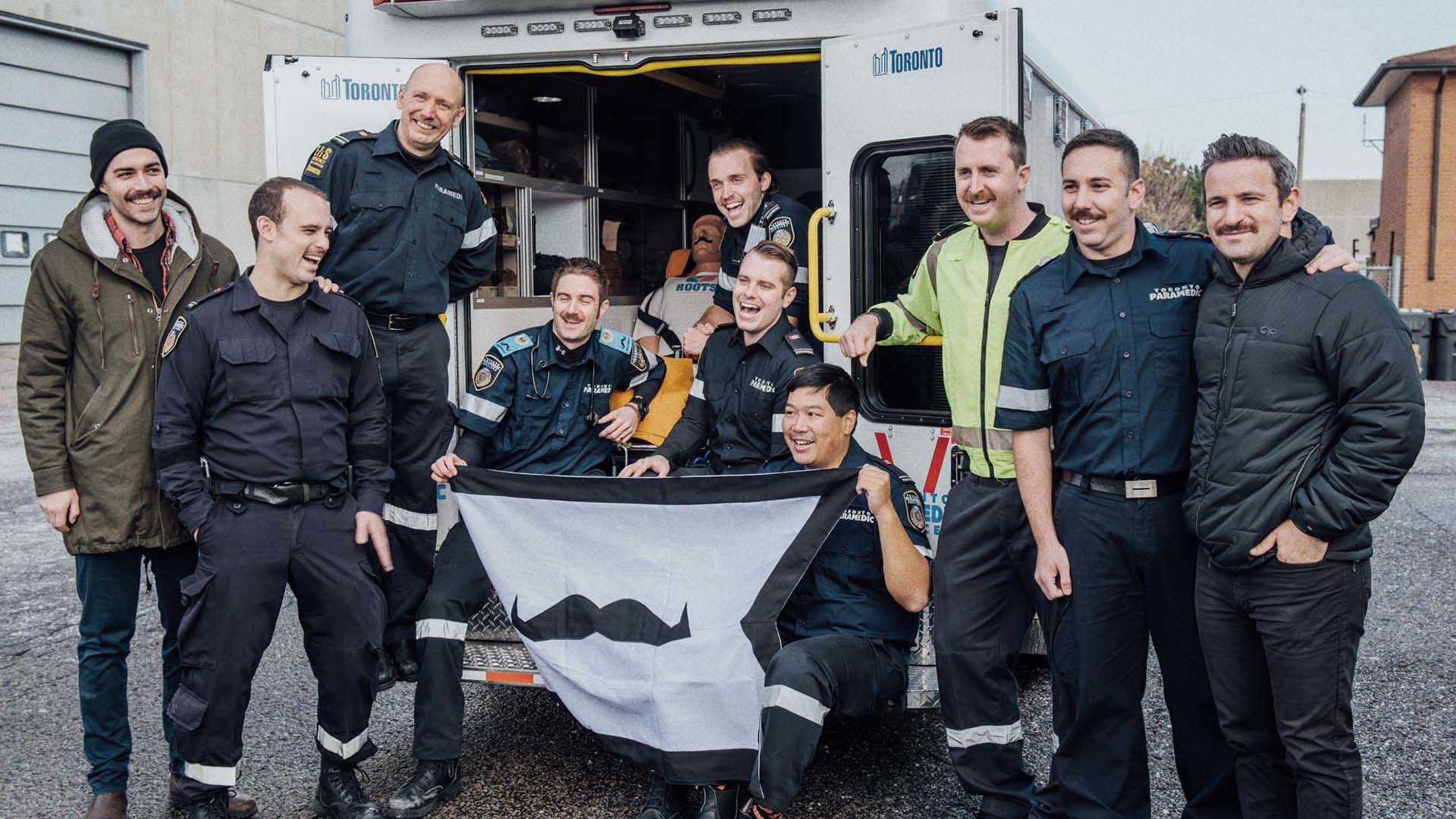 A photo of a group of emergency service workers with a moustache flag.