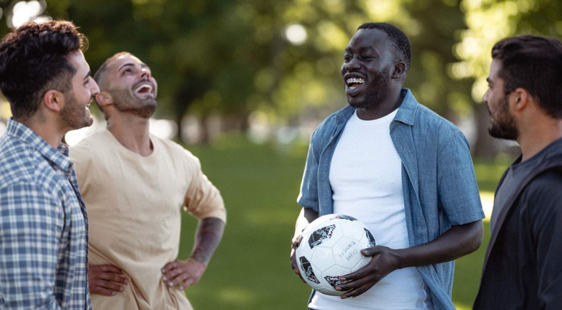 Four men standing in a park with a football laughing and having a good time