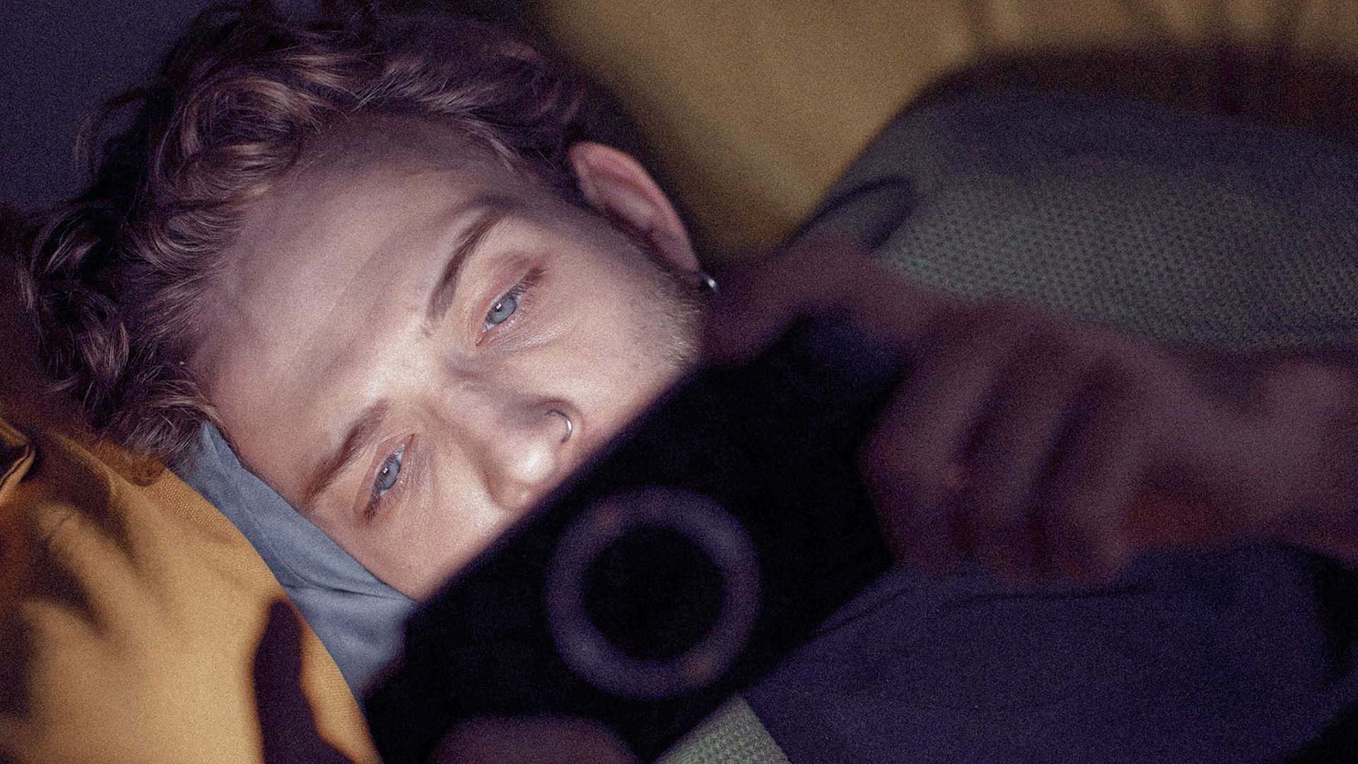 Photo of a young man lying down, engrossed on his smartphone.