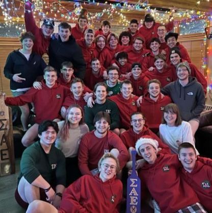 Photo of a group of College Students, posing to camera and wearing predominantly green and red Christmas attire.